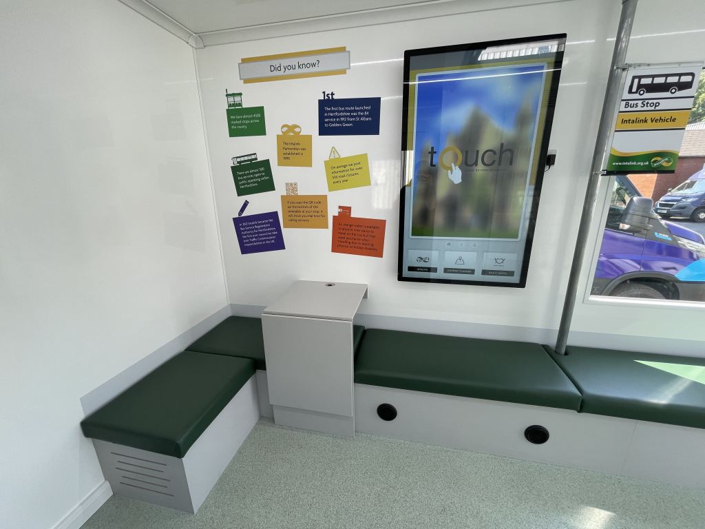 photo of the inside of the new intalink vehicle including green seating, drop-leaf table, bus stop complete with mini Intalink flag and interactive screen